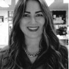 Smiling woman with long hair and necklace in a cozy indoor setting.